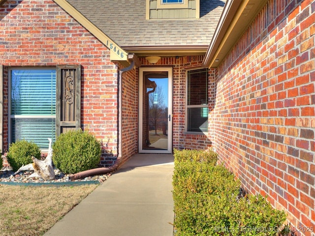 doorway to property featuring brick siding and a shingled roof