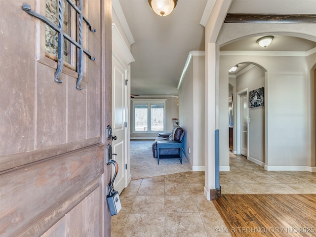 entryway featuring arched walkways, crown molding, baseboards, and light tile patterned floors