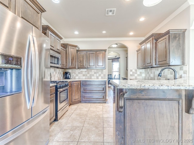 kitchen with arched walkways, light stone counters, light tile patterned flooring, visible vents, and appliances with stainless steel finishes