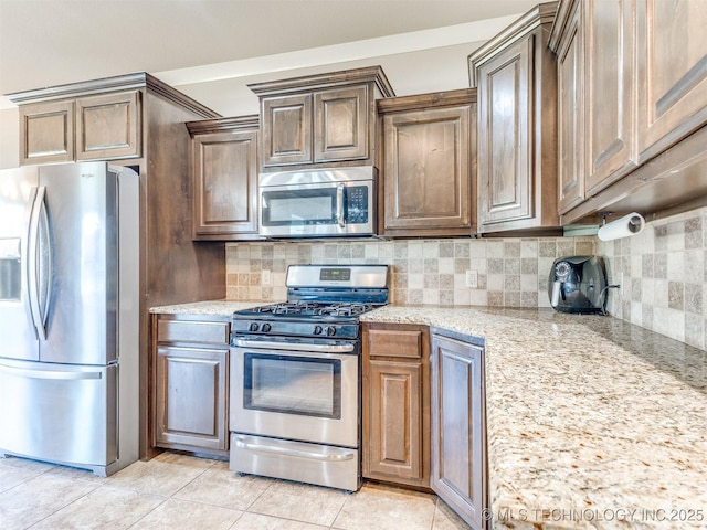 kitchen with appliances with stainless steel finishes, light tile patterned flooring, backsplash, and light stone countertops