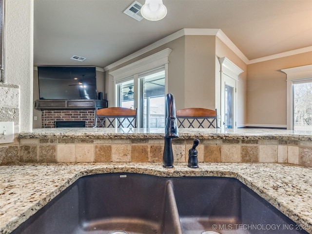 kitchen featuring light stone counters, a sink, visible vents, and crown molding