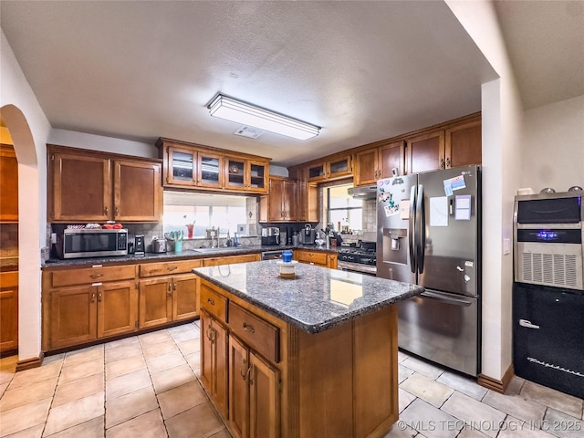 kitchen featuring under cabinet range hood, stainless steel appliances, a sink, a center island, and brown cabinets