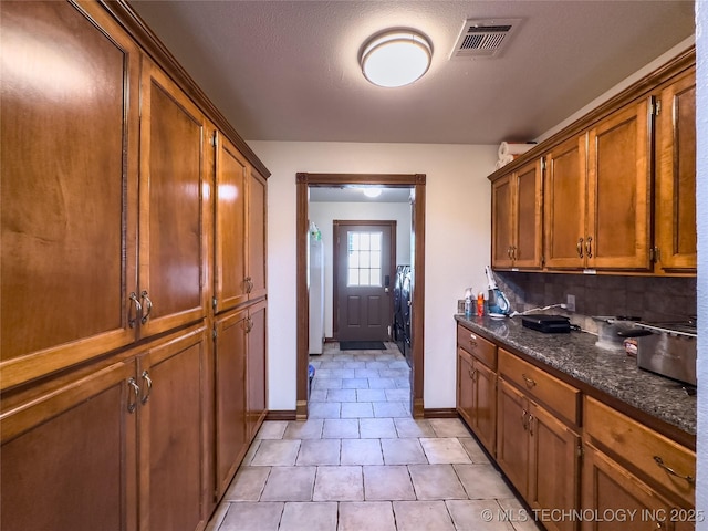 kitchen featuring light tile patterned floors, baseboards, visible vents, decorative backsplash, and brown cabinets