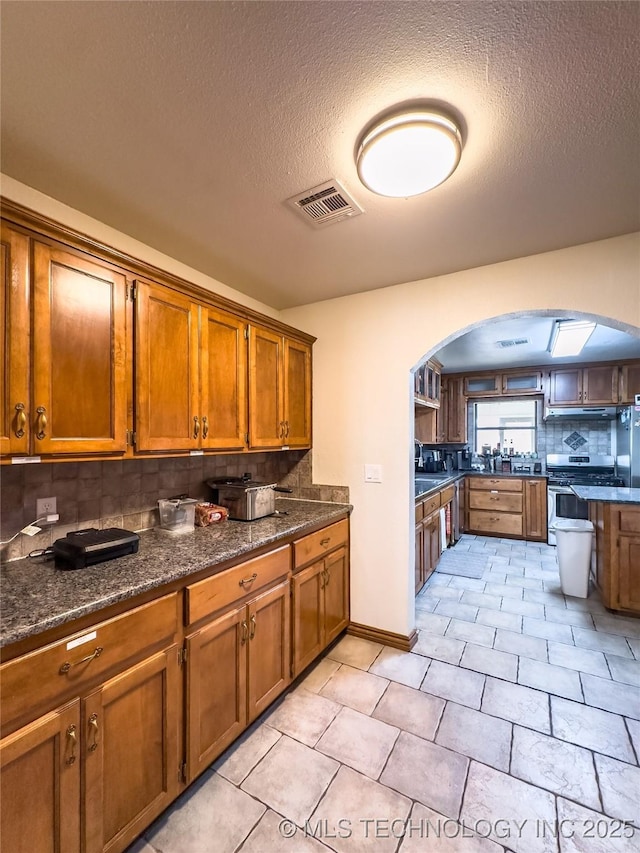 kitchen featuring brown cabinets, arched walkways, visible vents, and backsplash