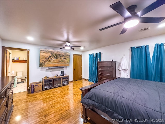 bedroom with a ceiling fan, ensuite bath, visible vents, and wood finished floors