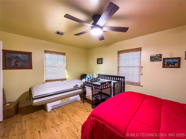 bedroom with a ceiling fan, visible vents, multiple windows, and wood finished floors