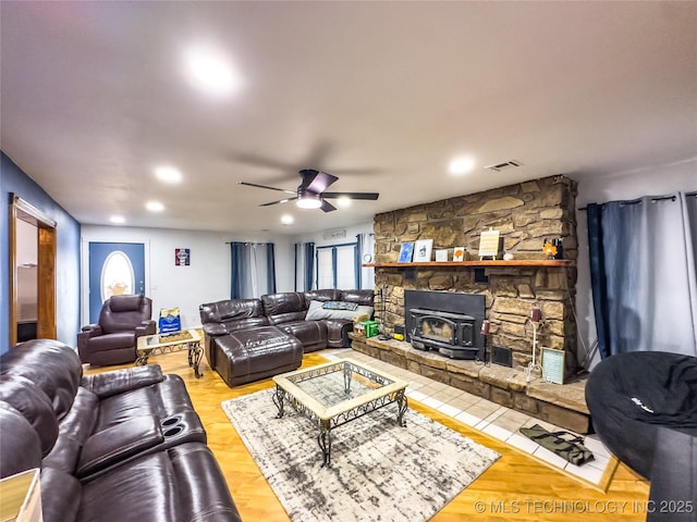 living area with a wood stove, ceiling fan, visible vents, and wood finished floors