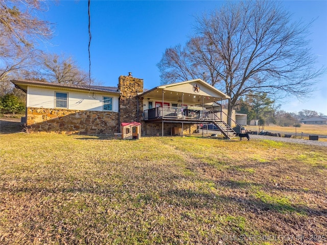 back of house featuring a deck, stone siding, stairway, a lawn, and a chimney