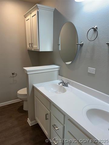 full bathroom featuring double vanity, wood finished floors, a sink, and toilet