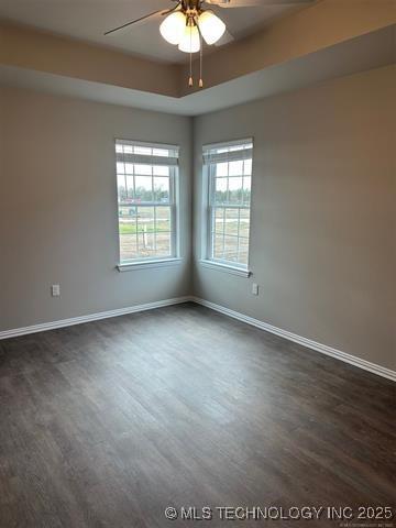 spare room with dark wood-style floors, a tray ceiling, and baseboards