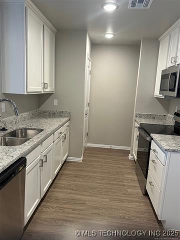 kitchen with stainless steel appliances, wood finished floors, a sink, and white cabinets