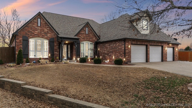 view of front of home featuring driveway, a shingled roof, an attached garage, fence, and brick siding