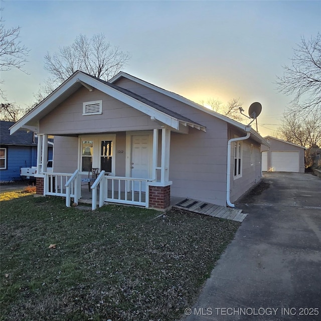 bungalow-style home featuring a garage, covered porch, a front lawn, and an outbuilding