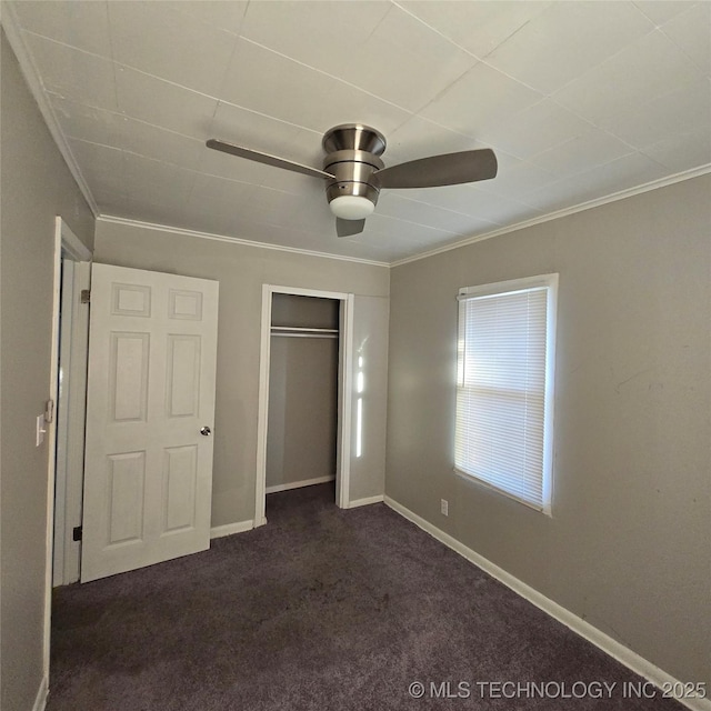 unfurnished bedroom featuring baseboards, a ceiling fan, ornamental molding, dark colored carpet, and a closet