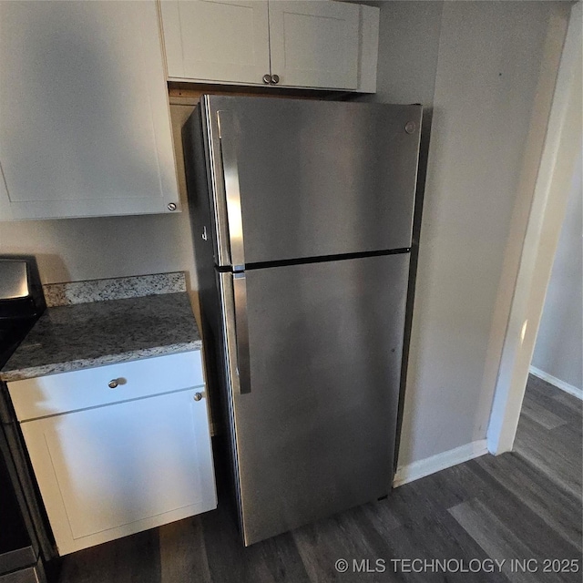 kitchen with light stone counters, electric stove, dark wood-style flooring, freestanding refrigerator, and white cabinetry