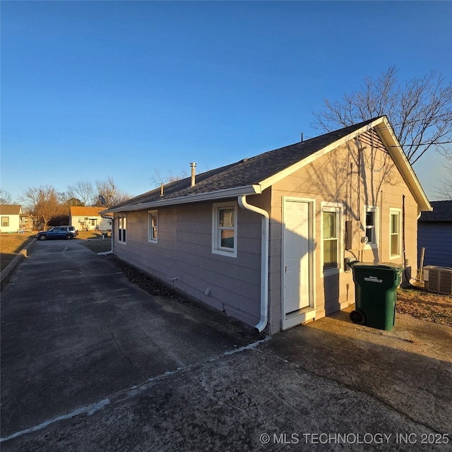 view of side of property with a shingled roof and cooling unit