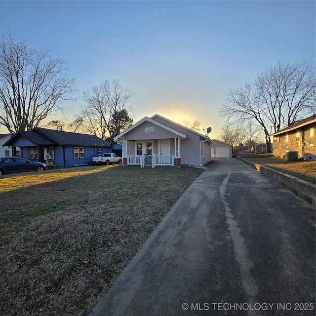 bungalow-style house featuring covered porch, a detached garage, central AC unit, and a front yard