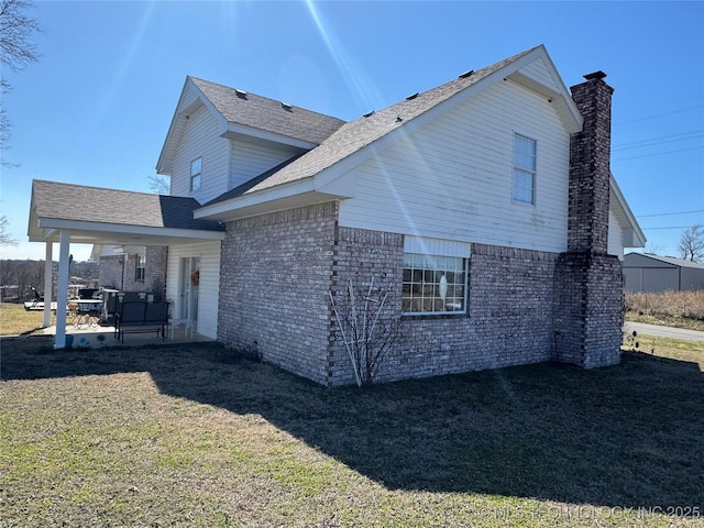 view of side of property with a chimney, brick siding, a lawn, and a patio area