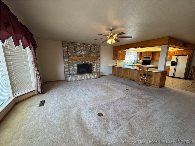 unfurnished living room featuring light carpet, visible vents, ceiling fan, a textured ceiling, and a fireplace