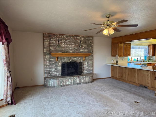 unfurnished living room with a textured ceiling, light colored carpet, a fireplace, a ceiling fan, and baseboards