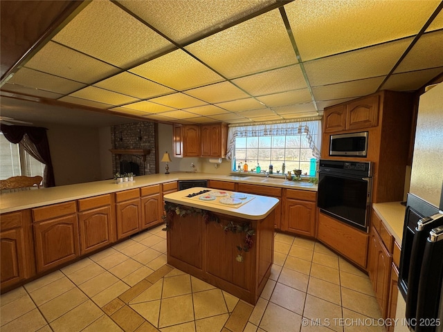 kitchen featuring light tile patterned floors, a paneled ceiling, a fireplace, light countertops, and black appliances