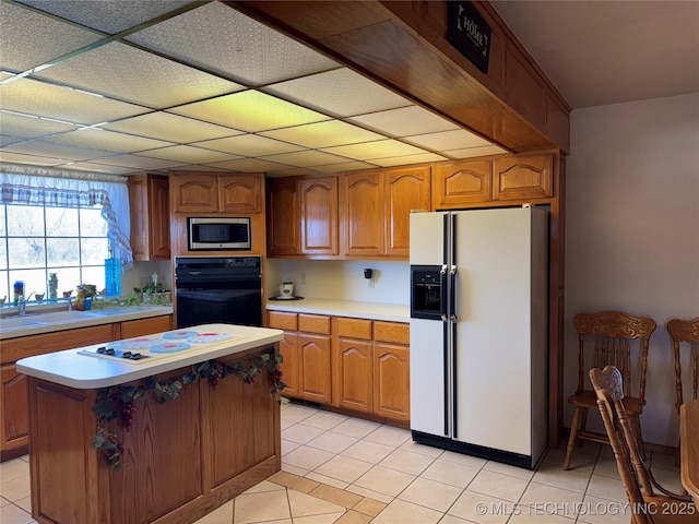 kitchen with white appliances, a sink, light countertops, brown cabinets, and a center island