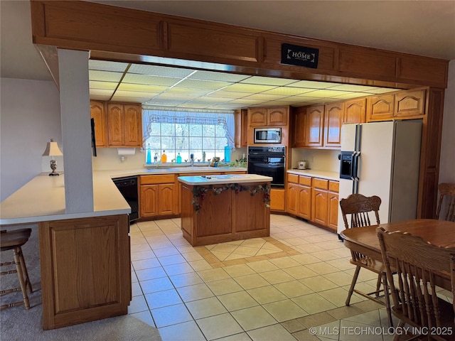 kitchen featuring light countertops, a kitchen island, black appliances, and light tile patterned floors