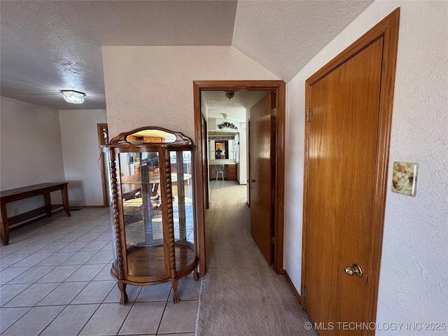 corridor featuring a textured ceiling, a textured wall, light tile patterned floors, and vaulted ceiling