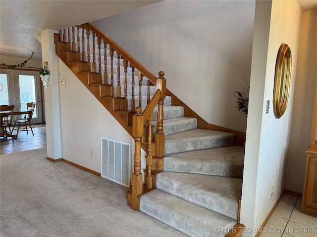 stairs with carpet floors, tile patterned flooring, visible vents, and baseboards