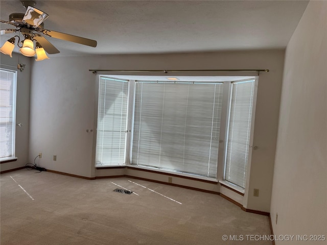 carpeted spare room with baseboards, visible vents, and ceiling fan