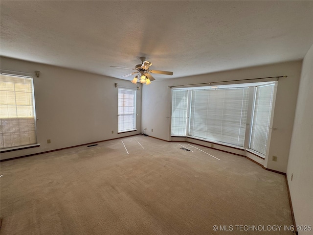 spare room featuring light carpet, a textured ceiling, a ceiling fan, and baseboards