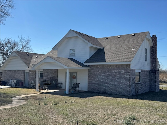 view of front of home featuring a shingled roof, a front yard, a patio area, and brick siding