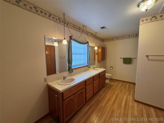 bathroom featuring double vanity, visible vents, a sink, and wood finished floors