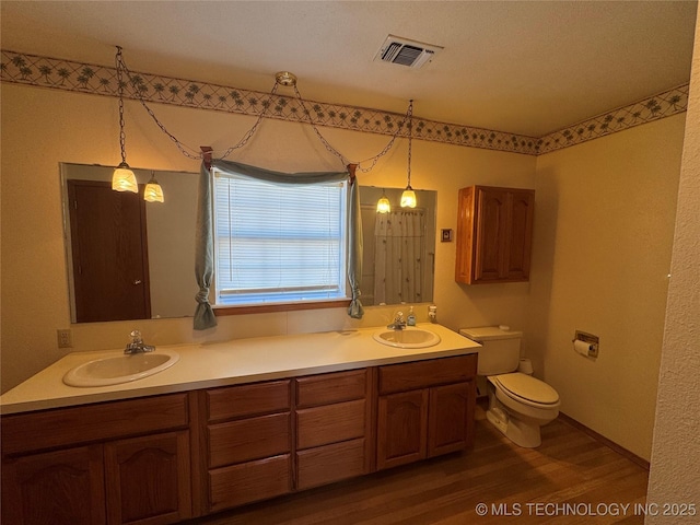 bathroom featuring toilet, double vanity, a sink, and visible vents