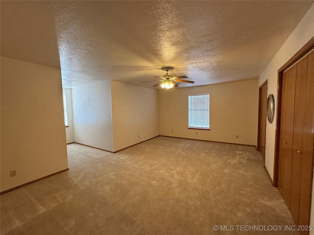 interior space with a textured ceiling, baseboards, a ceiling fan, and light colored carpet