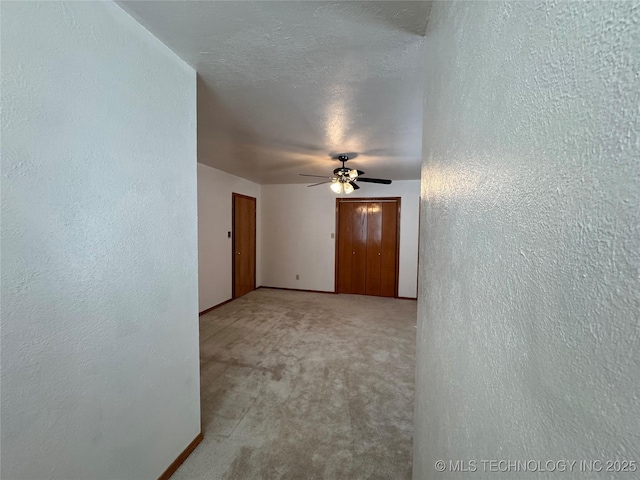 unfurnished room featuring baseboards, a textured wall, ceiling fan, carpet, and a textured ceiling