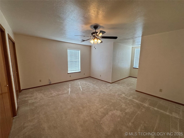 spare room with light carpet, a textured ceiling, baseboards, and a ceiling fan