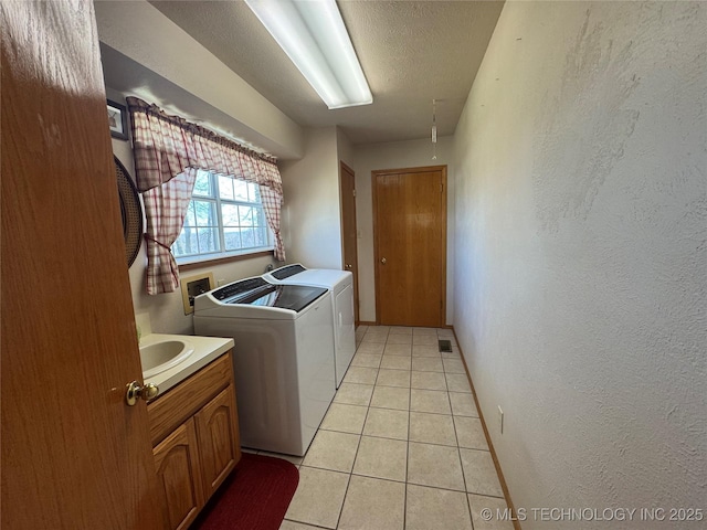 laundry room with washing machine and clothes dryer, light tile patterned floors, a textured wall, a textured ceiling, and laundry area