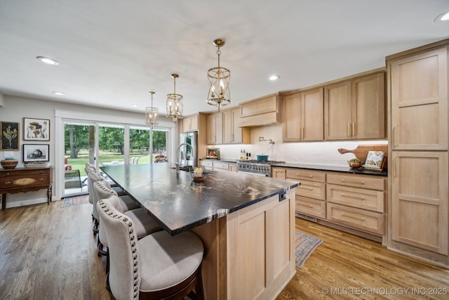 kitchen featuring a center island with sink, decorative backsplash, light brown cabinets, light wood-type flooring, and a kitchen bar