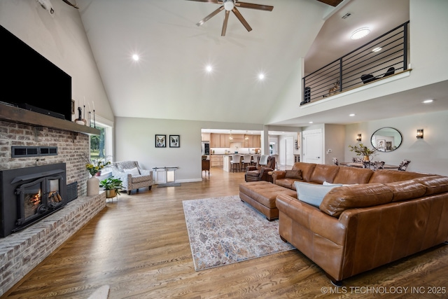 living room with high vaulted ceiling, wood finished floors, a ceiling fan, baseboards, and a brick fireplace