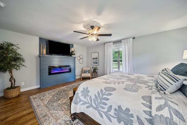 bedroom featuring ceiling fan, baseboards, wood finished floors, and a glass covered fireplace