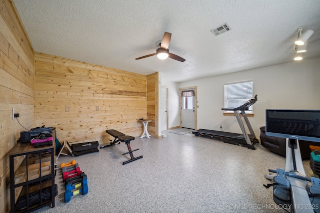 workout room featuring a ceiling fan, visible vents, wooden walls, and a textured ceiling