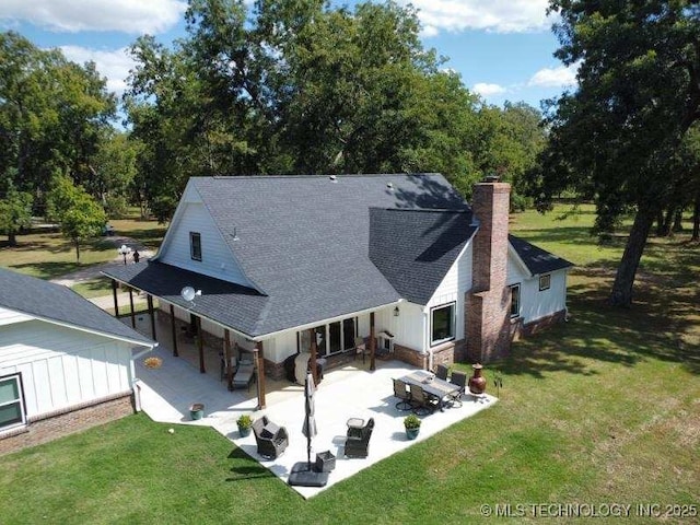 back of house with a patio area, a yard, a chimney, and roof with shingles