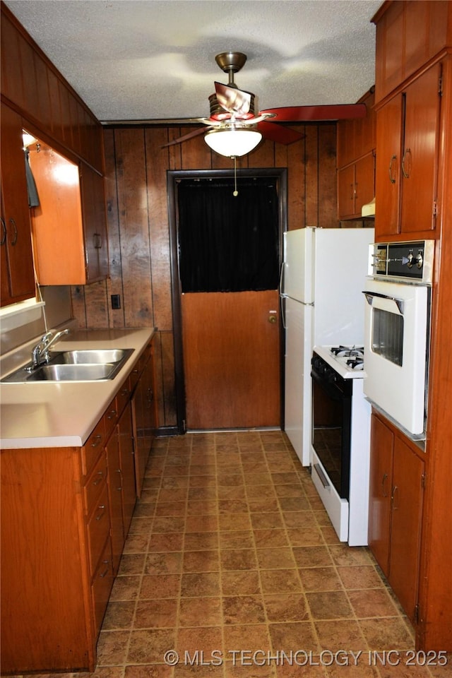 kitchen featuring range with gas cooktop, white oven, light countertops, wood walls, and a sink