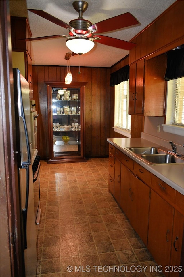 kitchen with stainless steel appliances, light countertops, a ceiling fan, a sink, and wood walls