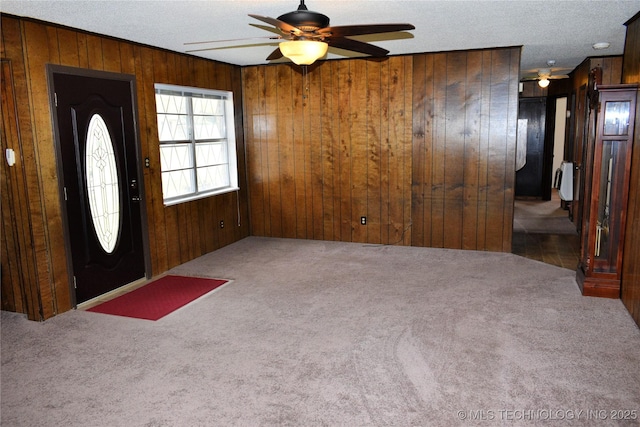 carpeted entryway with a textured ceiling, ceiling fan, wood walls, and heating unit