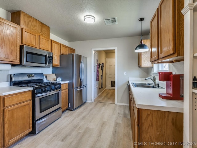 kitchen featuring visible vents, a sink, appliances with stainless steel finishes, brown cabinetry, and light countertops