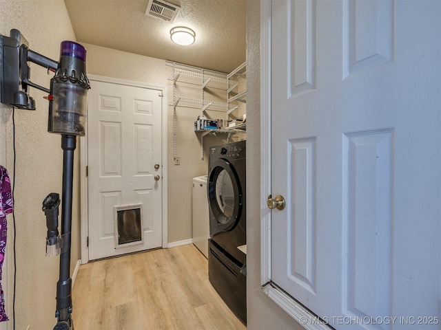 laundry room with visible vents, laundry area, washer / dryer, light wood-style floors, and a textured ceiling