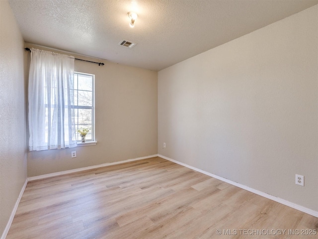 empty room with visible vents, light wood-type flooring, and a textured ceiling