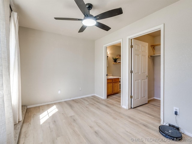 unfurnished bedroom with light wood-type flooring, a walk in closet, a ceiling fan, ensuite bathroom, and baseboards